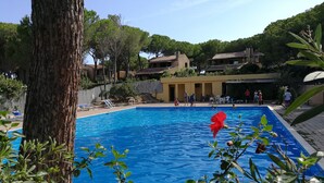 Une piscine à l’eau d’un bleu limpide, entourée de verdure et où se trouvent quelques personnes.
