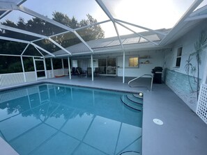 A swimming pool with a glass enclosure, a patio area with chairs, and a mural on the wall. - Heated pool for Your next vacation getaway! (North Port)