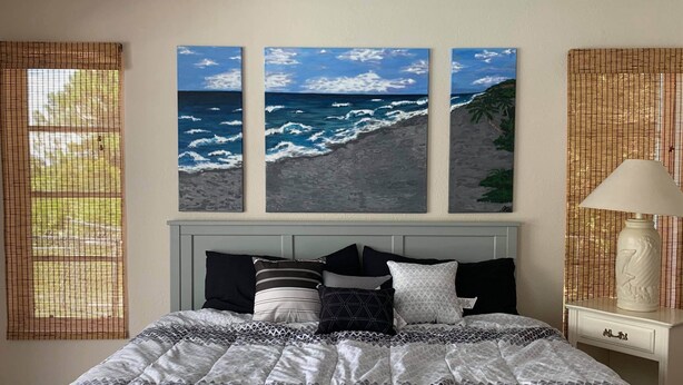 A bedroom with a bed, a nightstand, a lamp, and three wall-mounted paintings of the ocean. - Heated pool for Your next vacation getaway! (North Port)