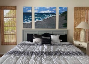 Un dormitorio con cama, mesita de noche, lámpara y tres cuadros colgados en la pared que representan el océano.