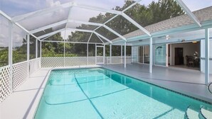 A covered swimming pool with a white lattice fence, clear blue water, and a view of the surrounding greenery. - Heated pool for Your next vacation getaway! (North Port)