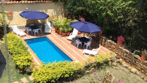 A backyard with a swimming pool, two umbrellas, and outdoor furniture. - La Buganvilla Barichara (Barichara)