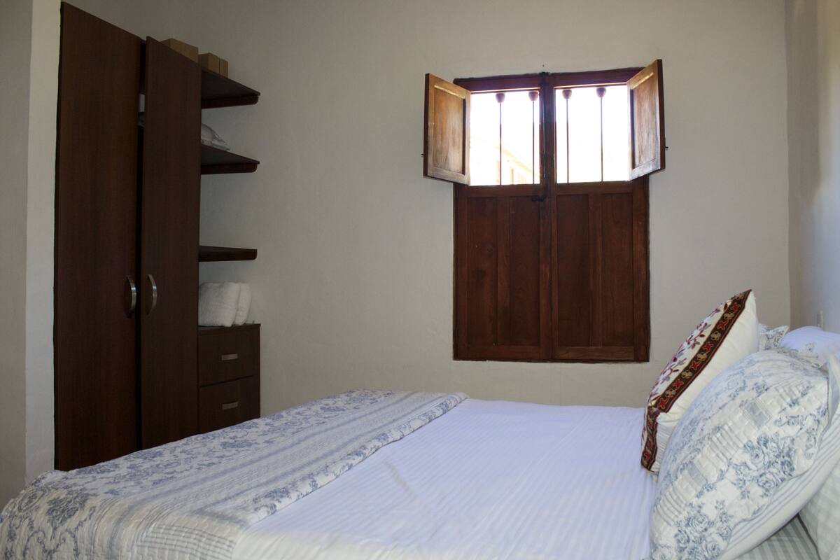 A bedroom with a bed, a wardrobe, and a window with wooden shutters.
