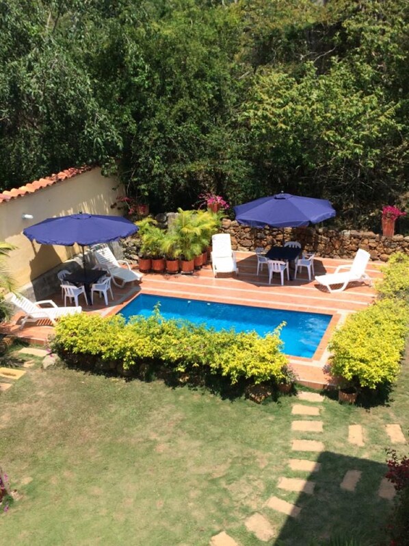 A backyard with a swimming pool, surrounded by potted plants and outdoor furniture. - La Buganvilla Barichara (Barichara)