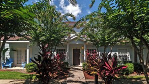 Una casa residencial con un porche delantero, una entrada de vehículos y un jardín.