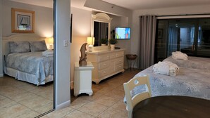 Habitación de hotel con cama, escritorio, silla, televisión y baño visible a través de una puerta de cristal.
