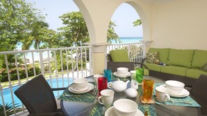 Un coin repas avec vue sur l’océan, un canapé vert et une table dressée avec des assiettes, des tasses et une théière.