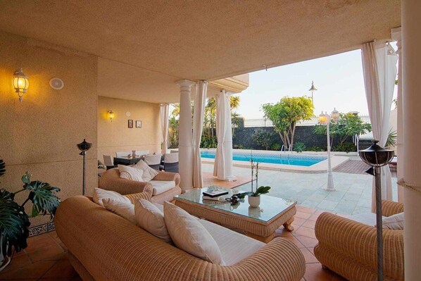 Un espacio exterior iluminado por el sol con mobiliario de mimbre, una piscina y vistas al paisaje.