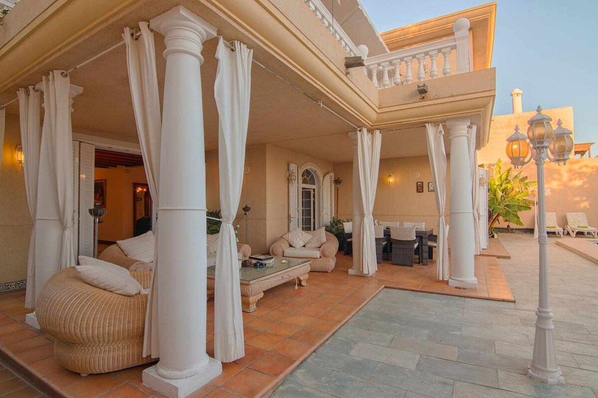 A covered outdoor seating area with columns, a sofa, and a table.