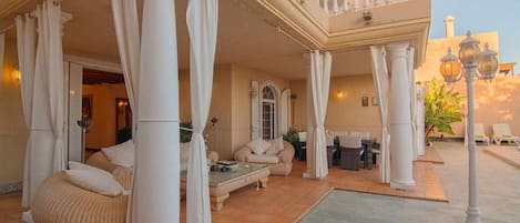 Un espacio al aire libre cubierto con columnas, un sofá y una mesa.