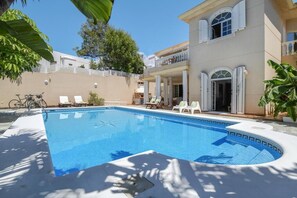 A swimming pool with lounge chairs and a bicycle, surrounded by a building with columns and a balcony. - Beachfront Ground-Floor Villa w/ Pool & BBQ (Playa Honda)