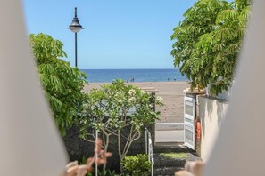 Blick auf einen Strand von einer überdachten Promenade aus, mit einer Laterne und Grünpflanzen.