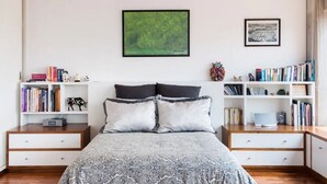 Une chambre à coucher avec un lit, deux tables de chevet, une bibliothèque et un tableau encadré au mur.