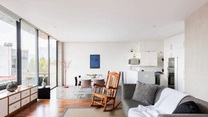 Un salon moderne avec un canapé gris, un fauteuil à bascule en bois et un coin repas comprenant une table et des chaises.