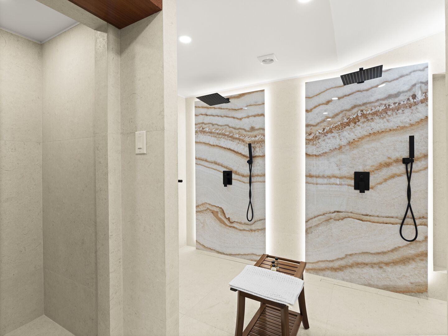 A modern bathroom with a marble wall, a wooden bench, and a shower area with a control panel.