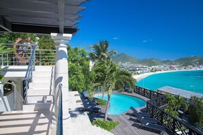 Ein Poolbereich mit Liegestühlen, einer Holzterrasse und Blick auf Strand und Berge.