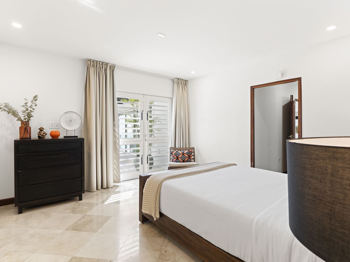 Quarto com cama, penteadeira, espelho e janela com cortinas.