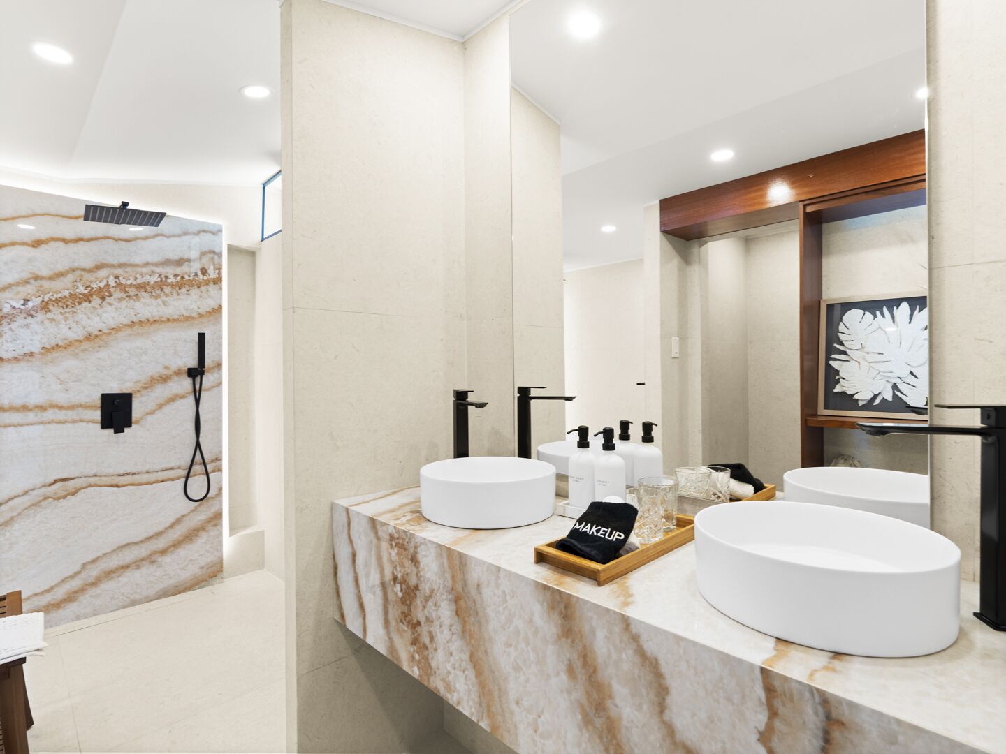 Une salle de bain moderne avec des comptoirs en marbre, deux lavabos, un grand miroir et un espace douche.