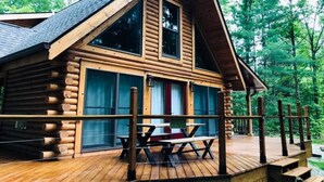 A log cabin with a wooden deck, large windows, and a picnic table. - Secluded, pet-friendly, new log cabin. (Morgantown)
