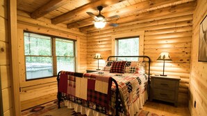 A cozy log cabin bedroom with a bed, two bedside tables, a ceiling fan, and large windows. - Secluded, pet-friendly, new log cabin. (Morgantown)