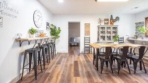 A modern kitchen with a wooden floor, black bar stools, a dining table with chairs, and a wall clock. - Pet-friendly, renovated, walk to downtown. (Nashville)