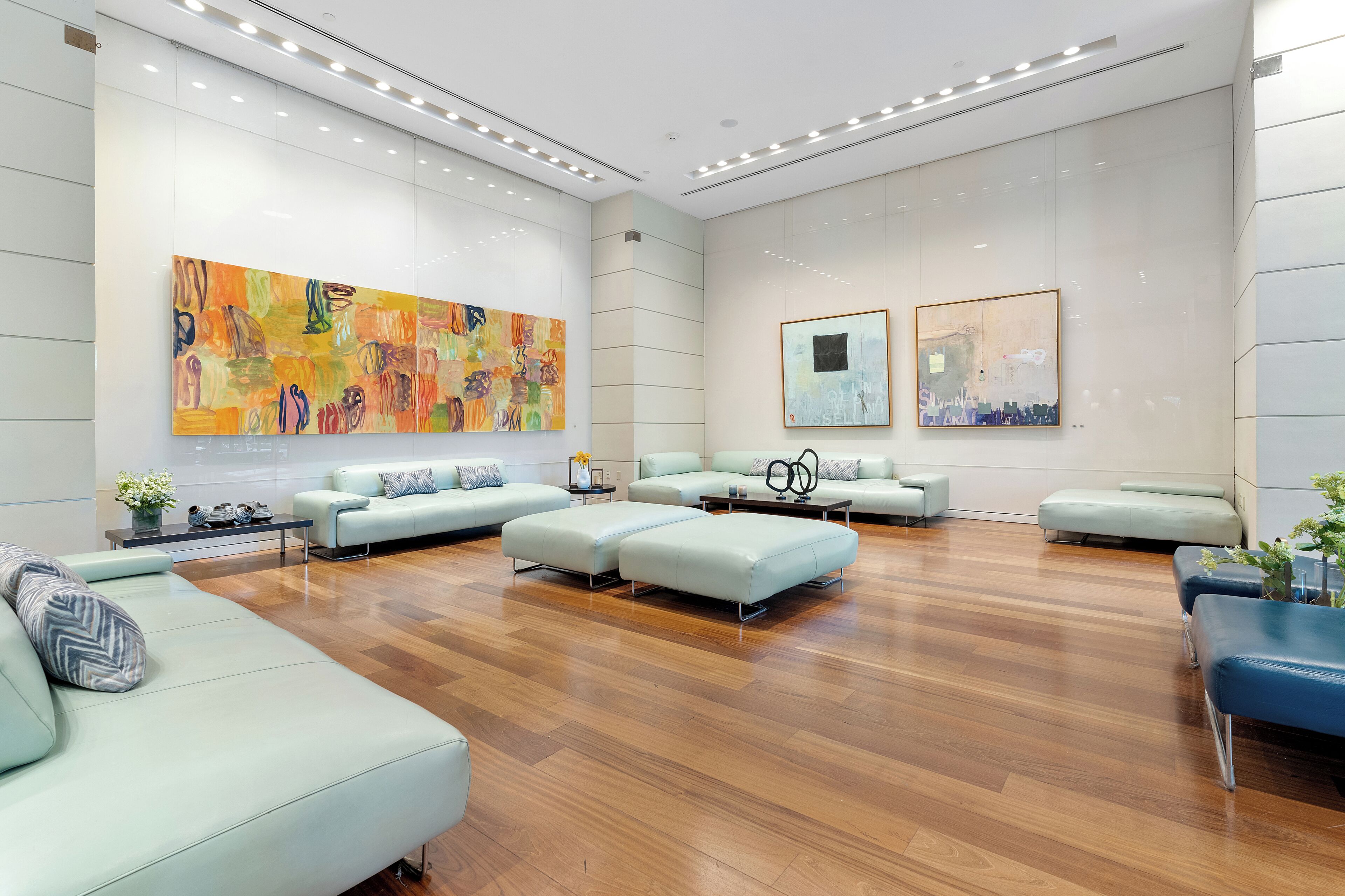 A spacious lobby with a wooden floor, multiple seating areas, and large abstract paintings on the walls.