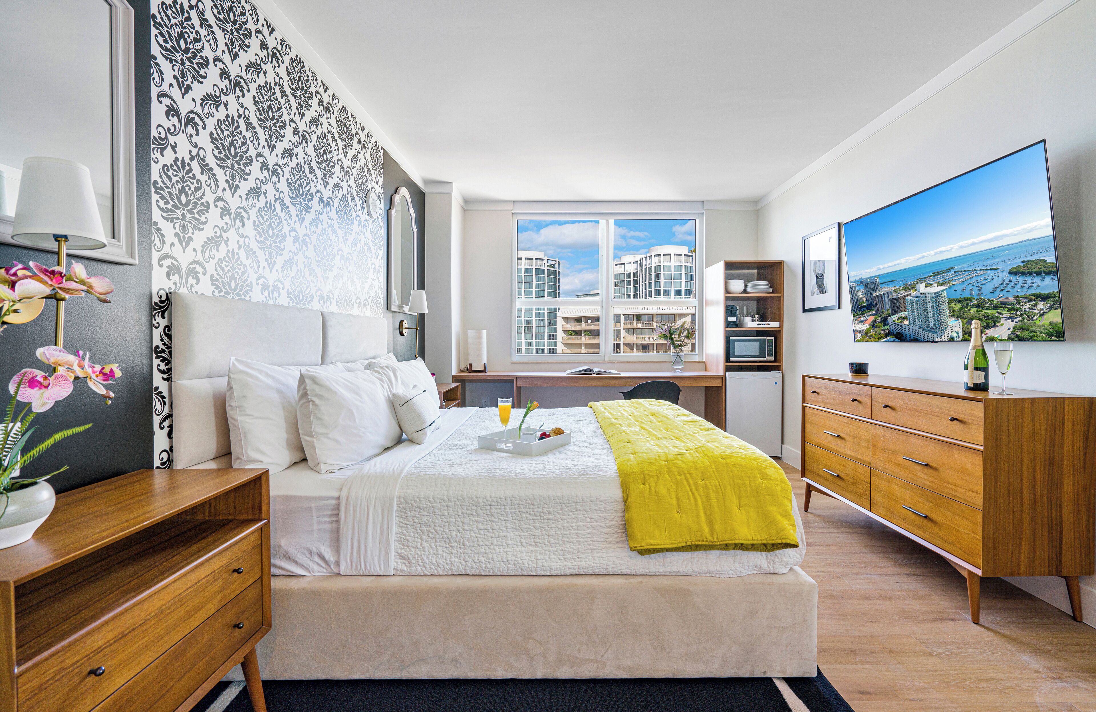 A modern hotel room with a large bed, a desk, a dresser, and a TV.