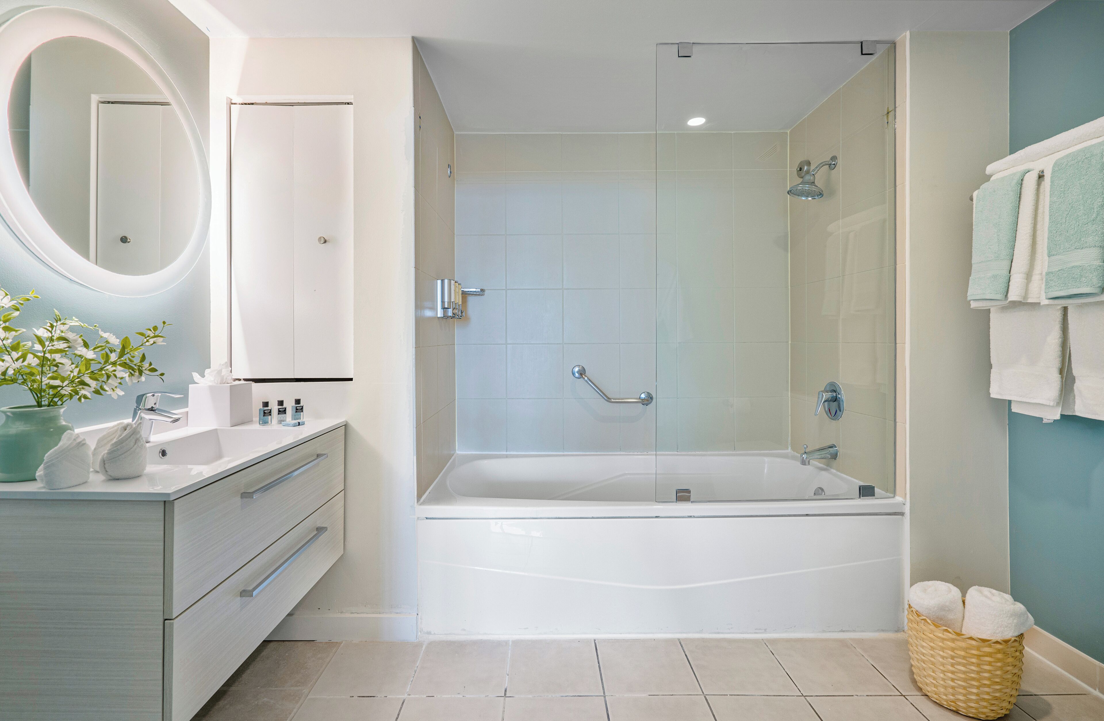 A modern bathroom with a bathtub, a shower, a vanity with a mirror, and a wicker basket with towels.