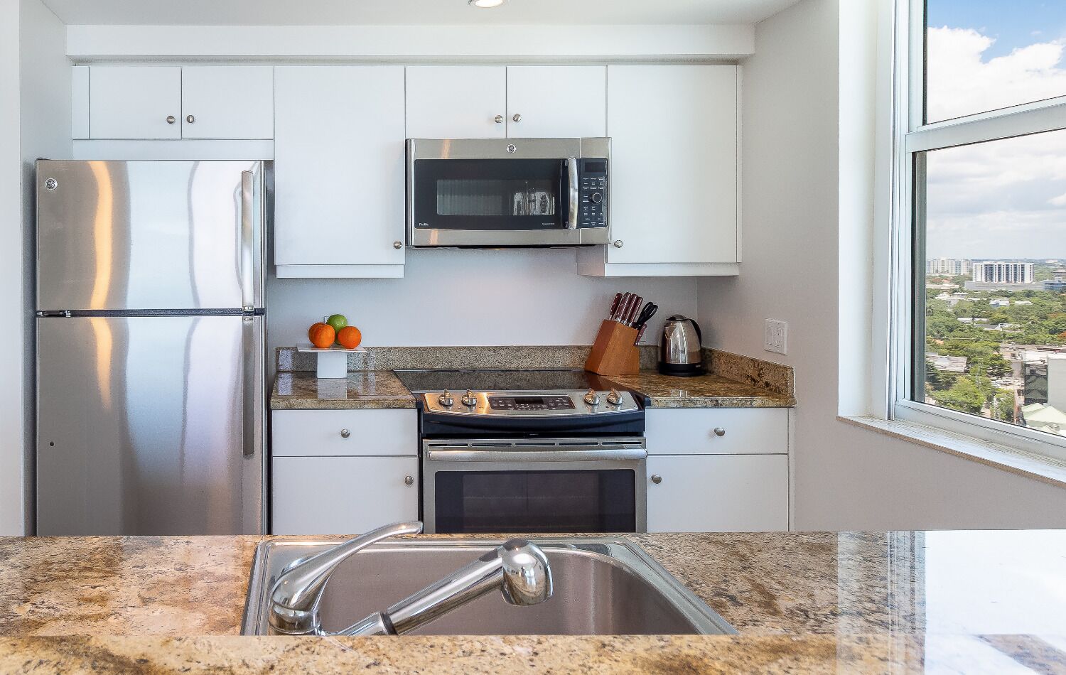 A modern kitchen with stainless steel appliances, white cabinets, and a granite countertop.
