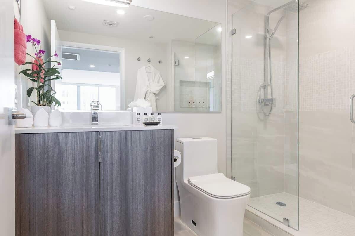 A modern bathroom with a glass-enclosed shower, a white toilet, and a wooden vanity.