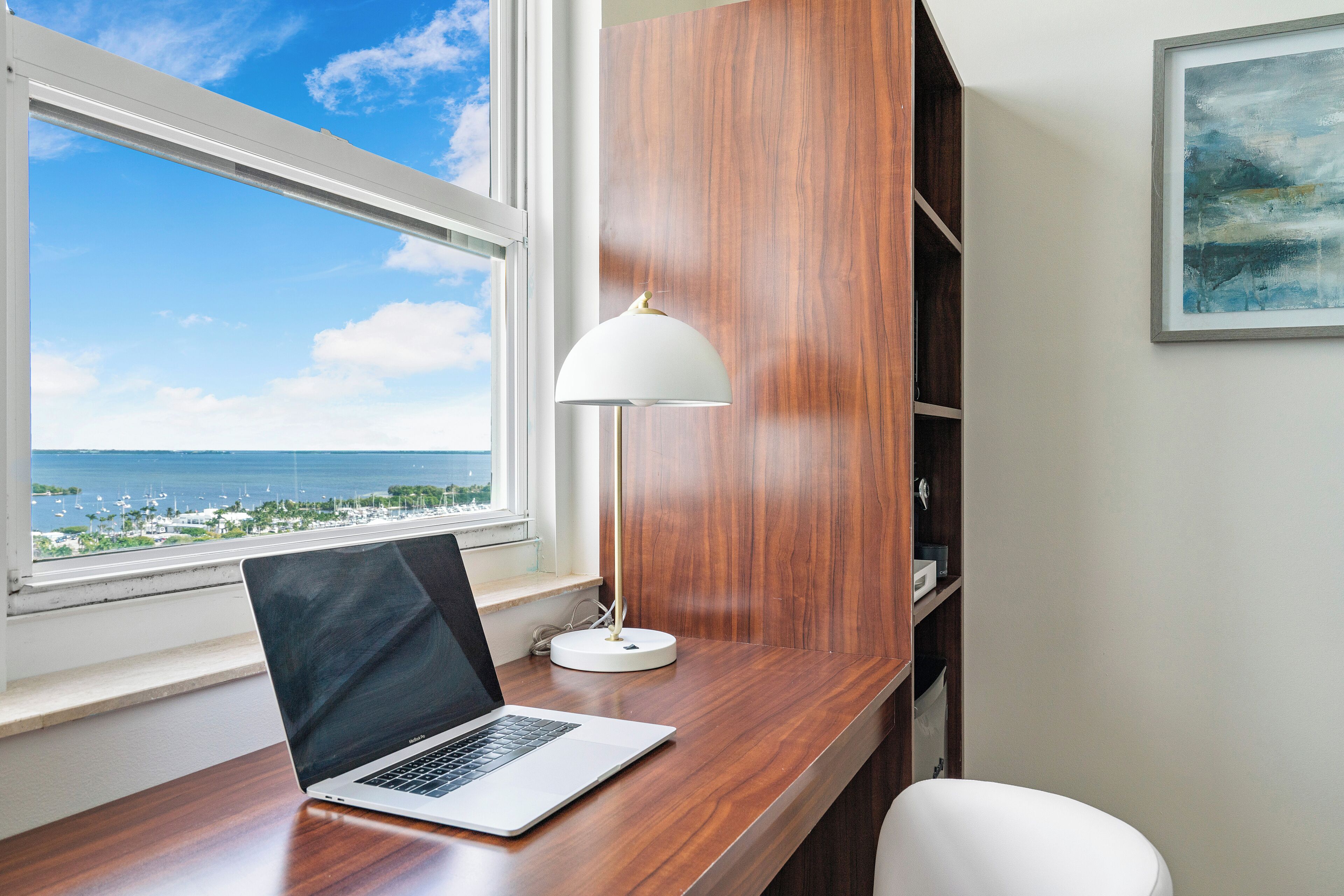 Um laptop sobre uma mesa de madeira junto a uma janela com vista para o mar.