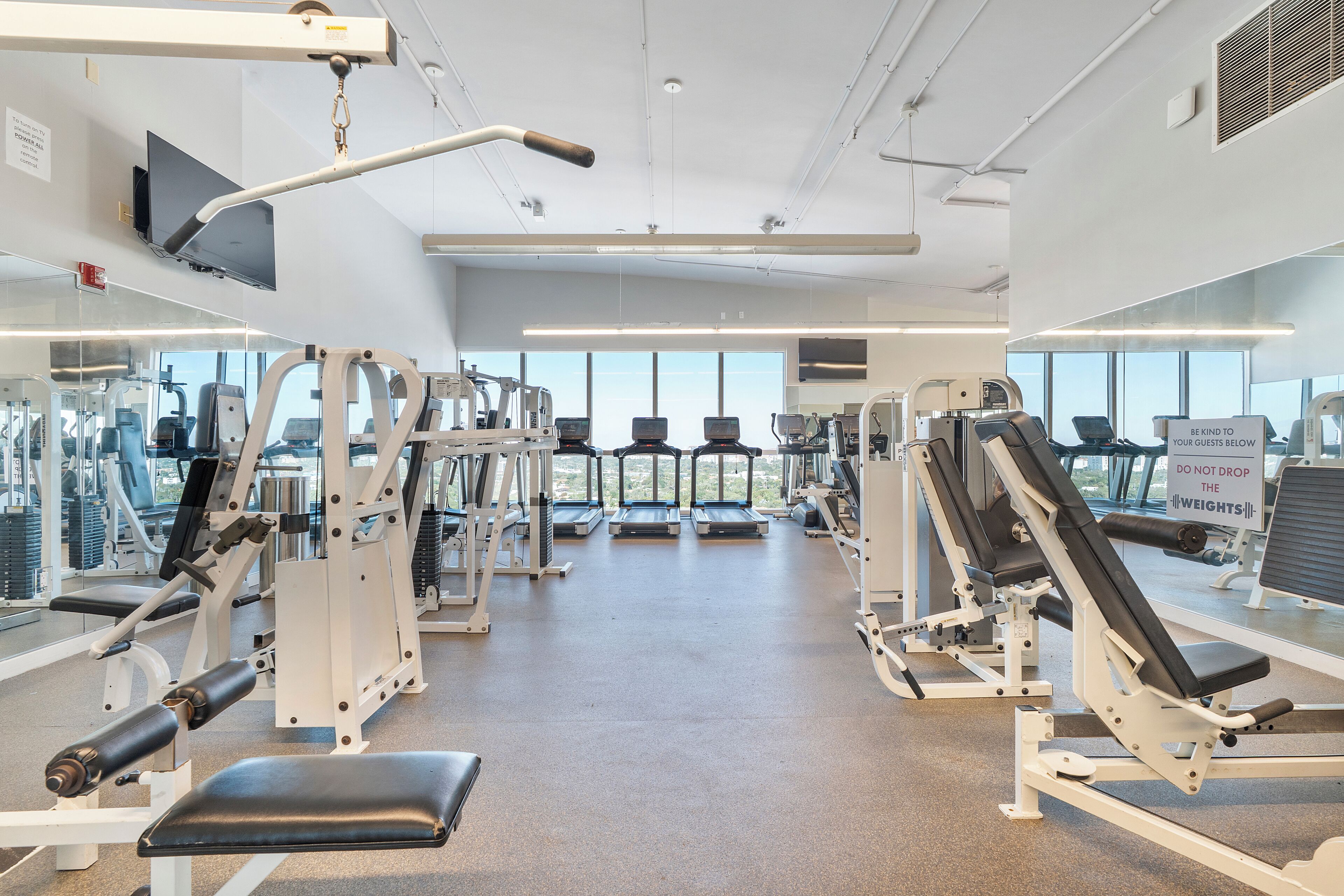 Een sportschool met diverse fitnessapparaten, loopbanden en een gewichtbank.