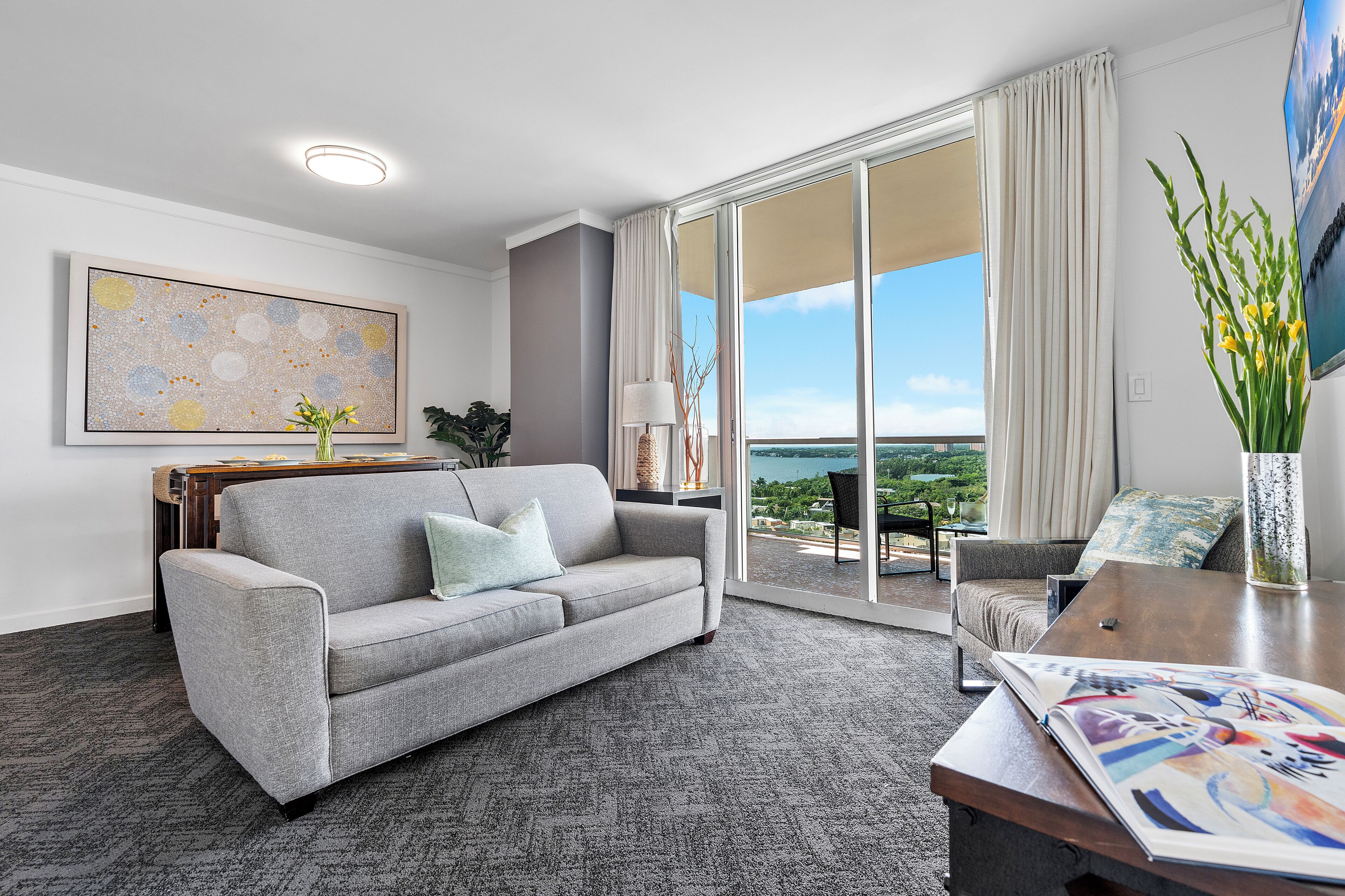 Un salon moderne avec un canapé gris, une table basse et une vue sur l’extérieur grâce à de grandes portes coulissantes.