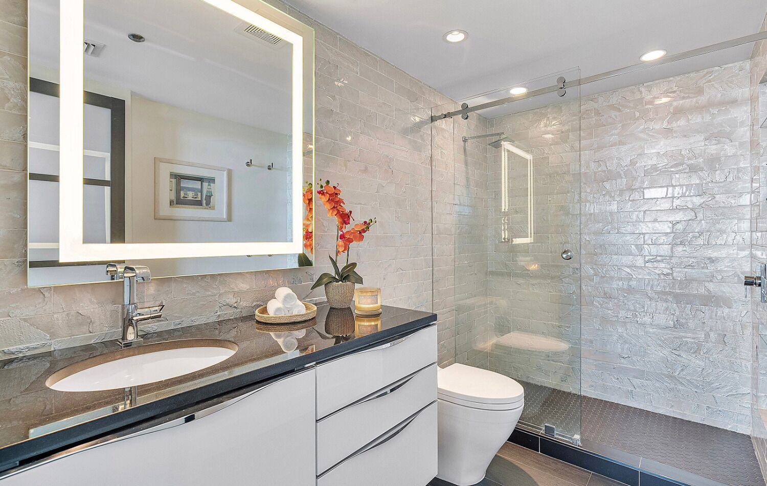 A modern bathroom with a large mirror, two sinks, a toilet, and a glass-enclosed shower.
