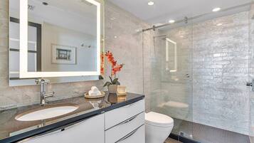 A modern bathroom with a large mirror, two sinks, a toilet, and a glass-enclosed shower.