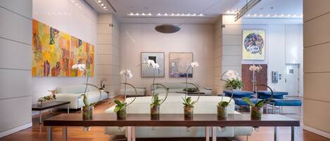 A modern interior with a wooden table, white sofas, and orchid plants.