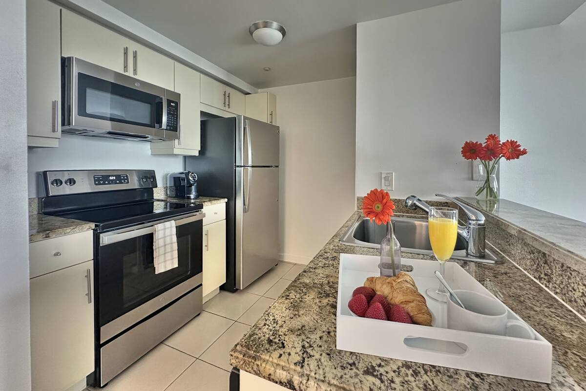 A modern kitchen with stainless steel appliances, a granite countertop, and a breakfast setup with croissants, strawberries, and orange juice.