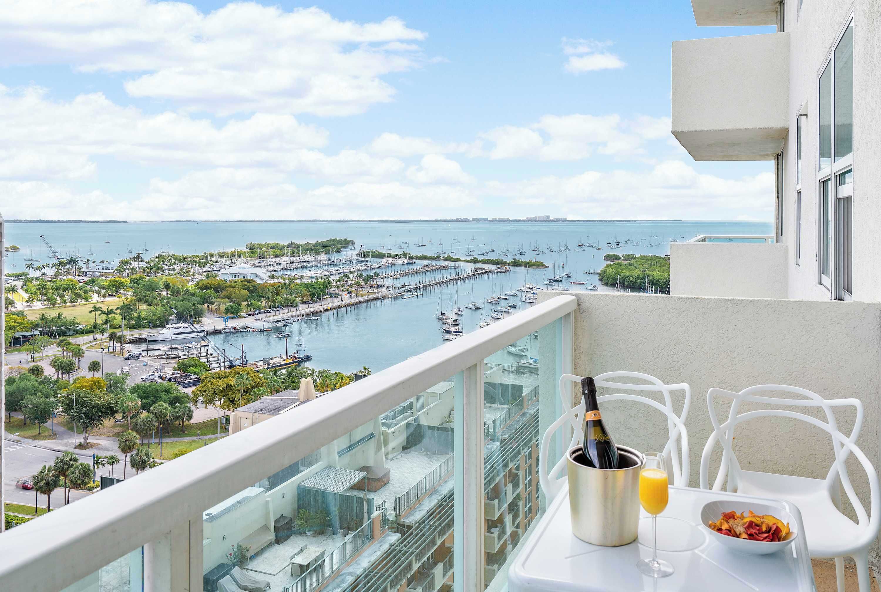 A balcony with a view of a marina, a bottle of champagne, and a glass of orange juice on a table.