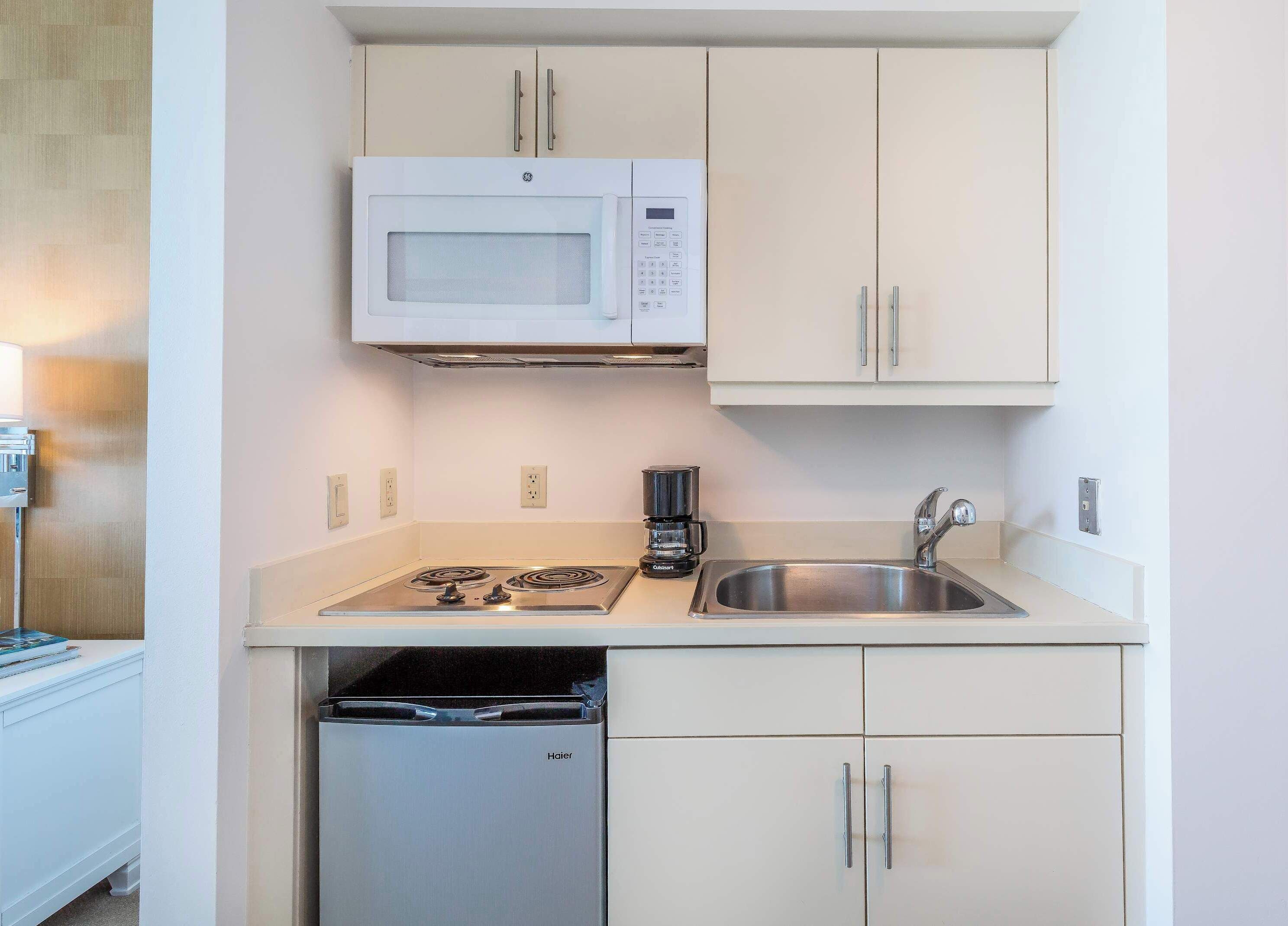 A compact kitchenette with a microwave, gas stove, coffee maker, sink, and dishwasher.