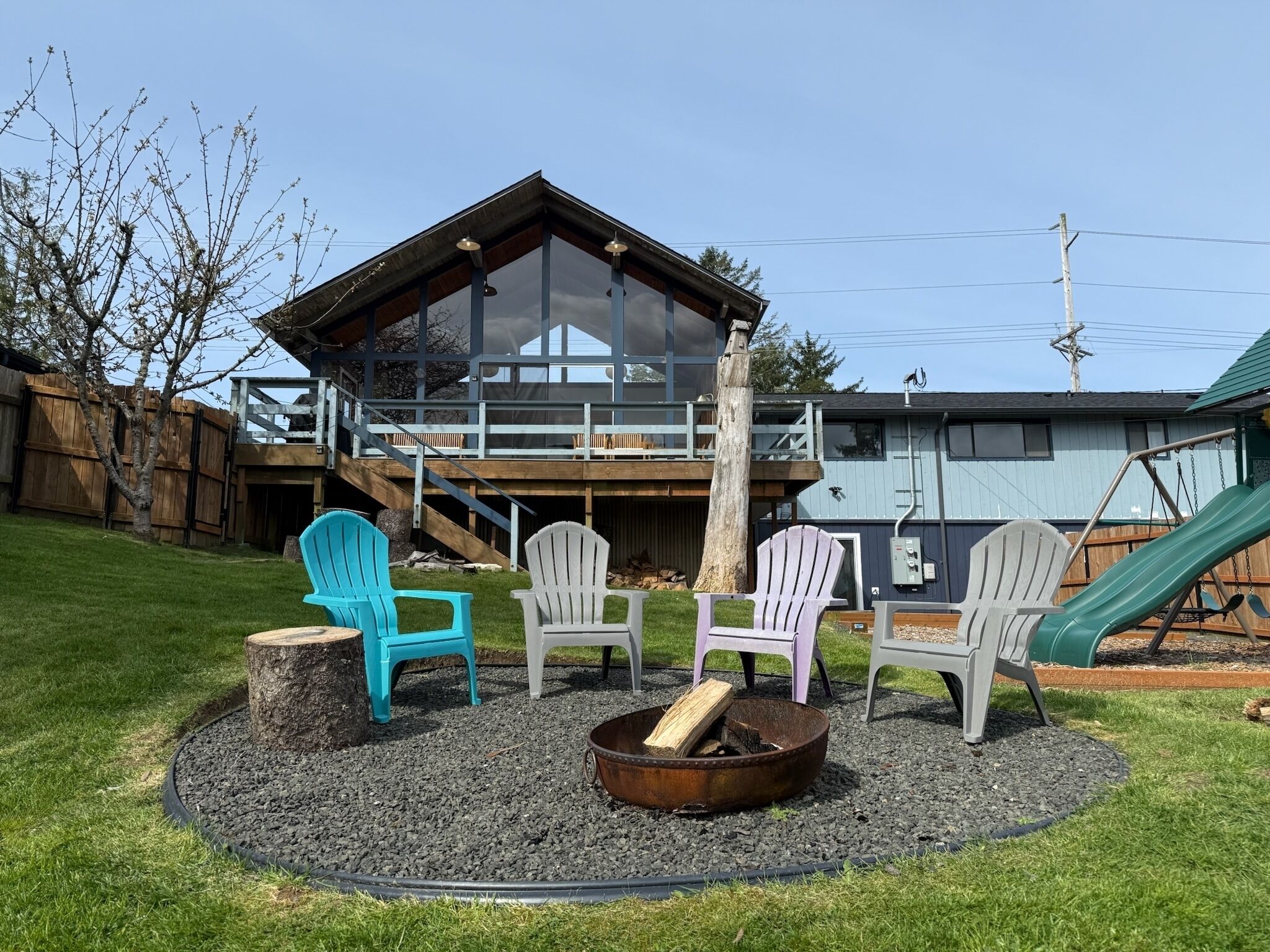 Un jardin avec un foyer, des fauteuils Adirondack, une terrasse en bois et un toboggan.