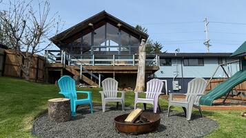 Un jardin avec un foyer, des fauteuils Adirondack, une terrasse en bois et un toboggan.