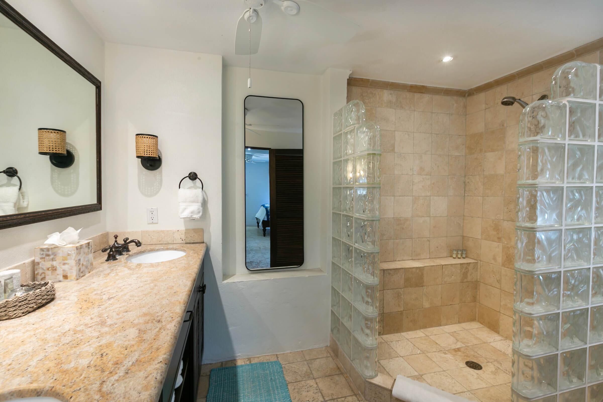 Une salle de bain dotée d’un comptoir en granit, de deux lavabos, d’un grand miroir et d’une cabine de douche en verre.