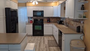 A compact kitchen with white cabinets, a black refrigerator, a microwave, a stove, and a dishwasher.