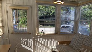 A cozy room with a wooden floor, a striped sofa, and a view of the street through large windows with blinds.