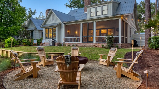 Ein Haus mit einer überdachten Terrasse, Adirondack-Stühlen und einem Feuerkorb.