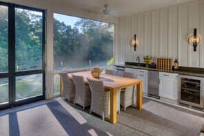 Una cocina moderna con un amplio ventanal, una mesa de comedor con sillas de mimbre y armarios blancos.