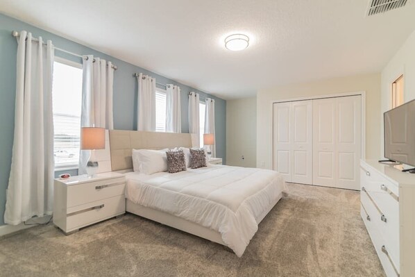 A bedroom with a bed, nightstands, a dresser, and a television.