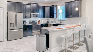 Une cuisine moderne avec des meubles de couleur sombre, des appareils en acier inoxydable, un îlot central doté de tabourets et une poubelle.