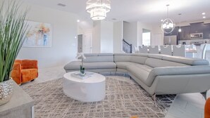 Un salon moderne avec un canapé d’angle gris, une table basse blanche et un tapis à motifs.
