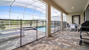 Un patio couvert avec vue sur une piscine, un espace salon extérieur et un barbecue.